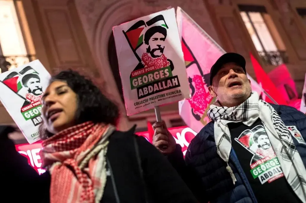 محتجون يحملون لافتات تطالب بالإفراج عن الناشط جورج إبراهيم عبد الله، مع وجود علم فلسطين، في تظاهرة تضامنية.