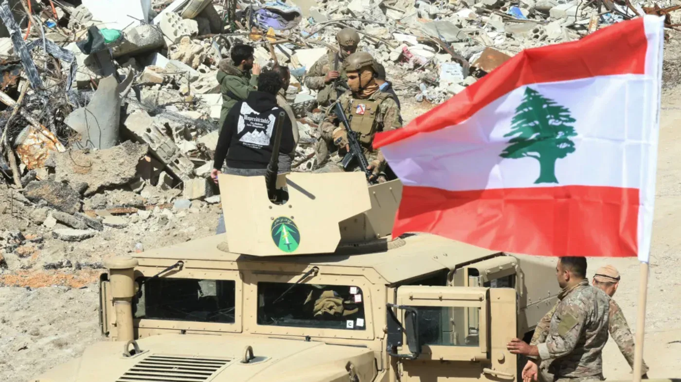 جنود لبنانيون يحملون العلم اللبناني في منطقة مدمرة، في سياق التوترات السياسية والاقتصادية في لبنان.