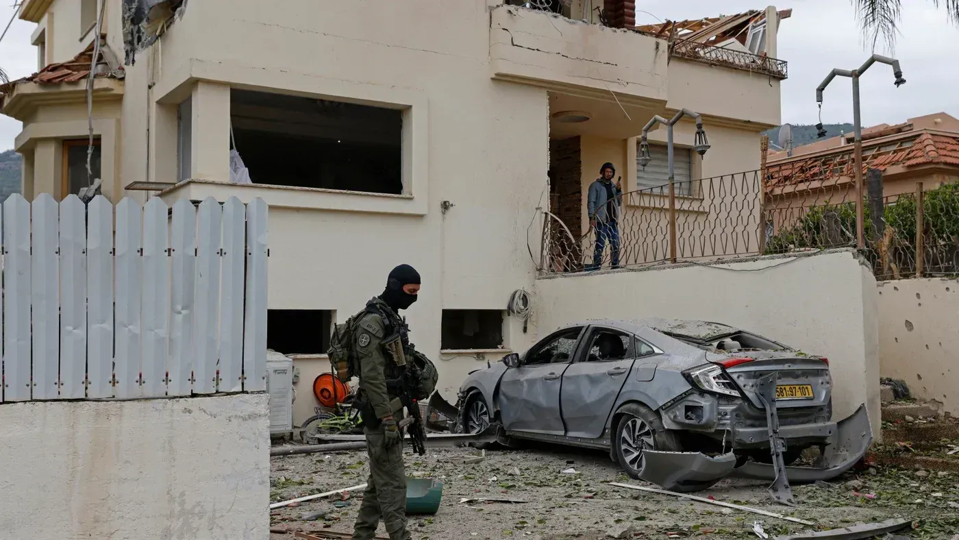 مقاتل من حزب الله يقف أمام منزل مدمر وسيارة متضررة، في سياق التصعيد العسكري على الحدود اللبنانية الإسرائيلية.