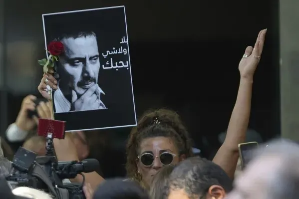 محتجون يحملون لافتة تحمل صورة زياد الرحباني مع وردة، في تجمع لتكريمه بعد وفاته، معبرة عن الحزن والاحترام.