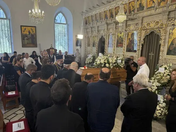 تجمع حشد من الناس في كنيسة لتقديم العزاء للملحن زياد الرحباني، حيث يظهر النعش محاطًا بالزهور والناس في حالة تأمل.