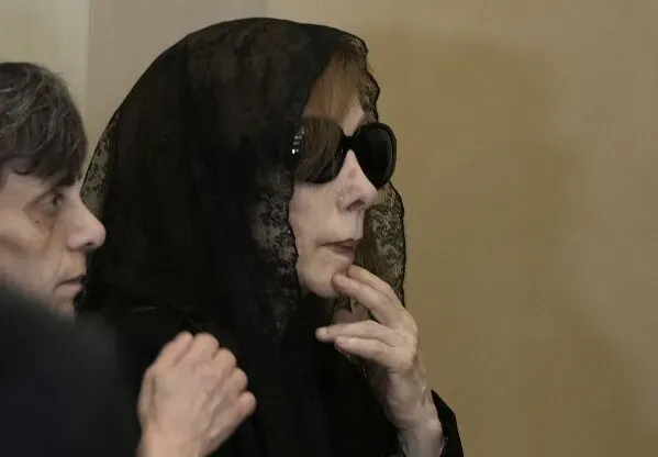 فيروز، ترتدي حجابًا أسود ونظارات شمسية، تظهر في مناسبة تأبين ابنها زياد الرحباني، محاطة بالمعزين في لحظة حزينة.