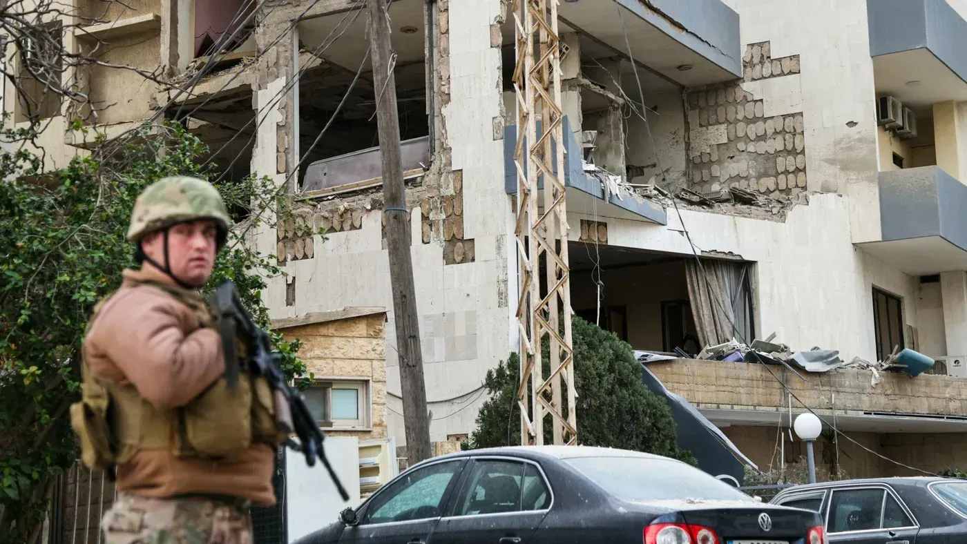 جندي لبناني يقف أمام مبنى متضرر من القصف، مما يعكس التوترات المستمرة بين الجيش وحزب الله في ظل الصراع الإسرائيلي اللبناني.