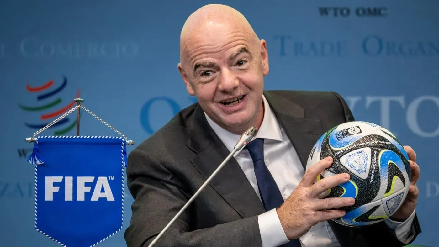 جياني إنفانتينو، رئيس الفيفا، يحمل كرة قدم بجانب شعار الفيفا، خلال مؤتمر صحفي يتناول قضايا رياضية دولية.