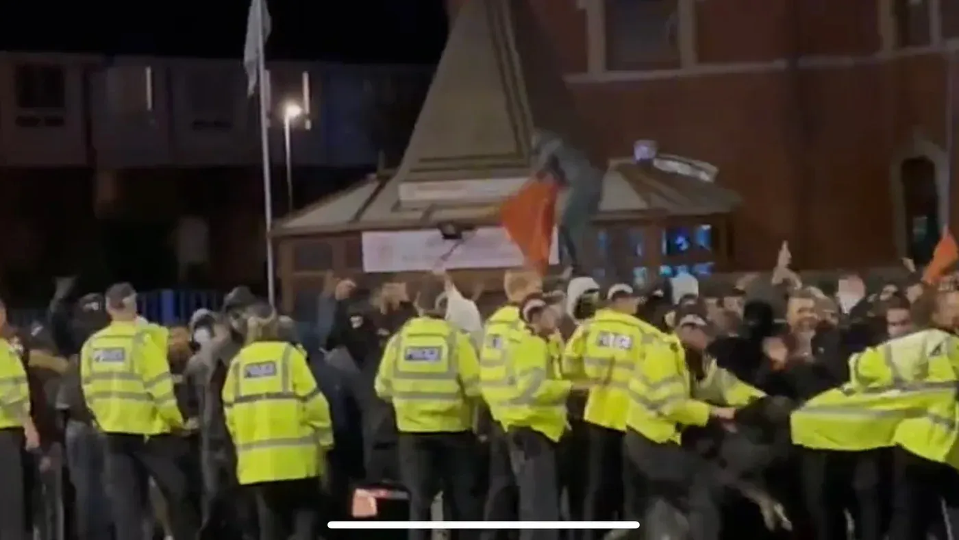 اشتباكات بين الشرطة ومحتجين في ليستر، حيث يظهر ضباط يرتدون سترات صفراء وسط حشود متوترة، تعكس تصاعد العنف الطائفي في 2022.