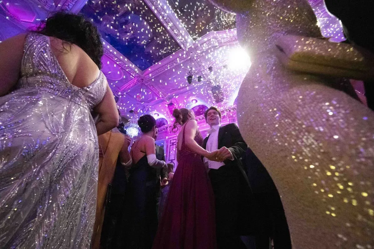 حضور مجموعة من الضيوف يرتدون فساتين سهرة أنيقة في حفل راقص في فيينا، مع أضواء ملونة تتلألأ في السقف.