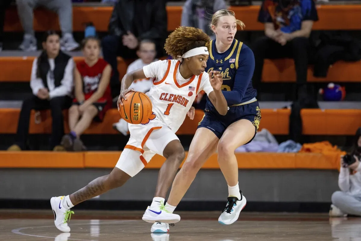 لاعبة كرة سلة من فريق كليمسون تت dribble الكرة بينما تتصدى لها لاعبة من نوتردام، في مباراة تنافسية بين الفريقين.