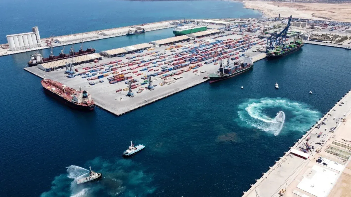 تظهر الصورة منظرًا جويًا للمنطقة الحرة في مصراتة، مع سفن وشاحنات حاويات، تعكس التوسع الاقتصادي والاستثماري في ليبيا.