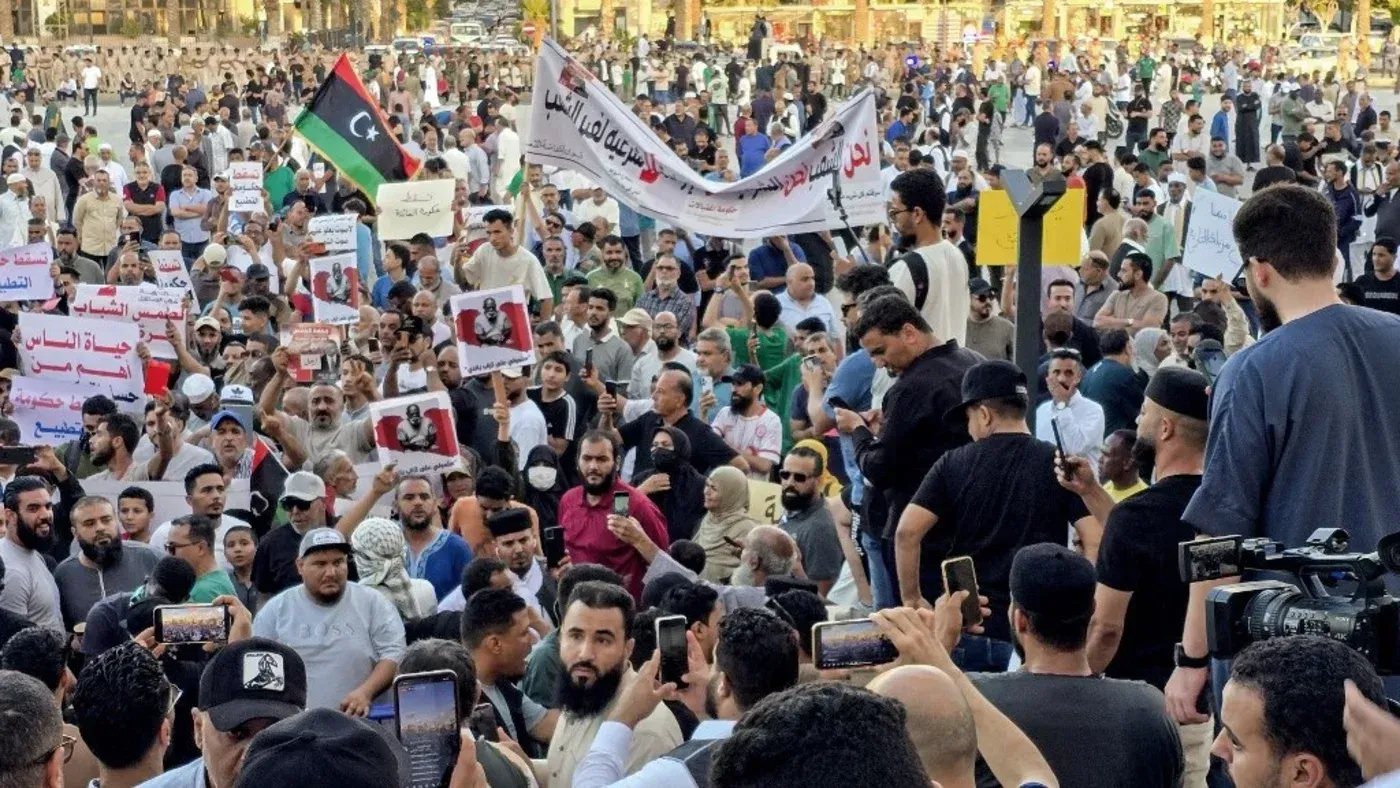 مظاهرة حاشدة في ليبيا، حيث يحمل المشاركون لافتات تعبر عن مطالبهم السياسية، مع تواجد العلم الليبي في الخلفية.
