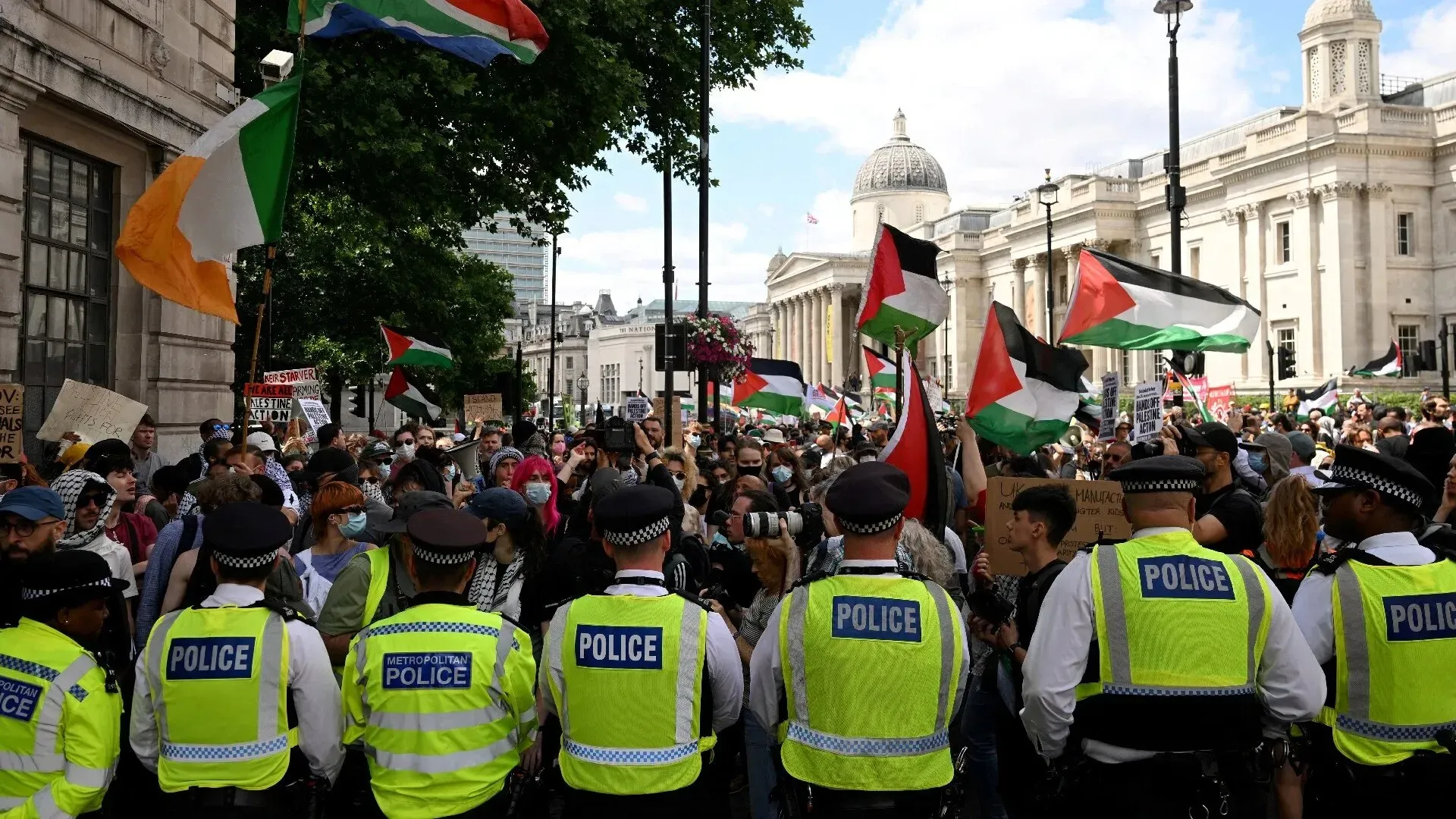 تجمع حشود من المتظاهرين في لندن يحملون الأعلام الفلسطينية، بينما يقف رجال الشرطة أمامهم، مما يعكس التوتر بين النشطاء والسلطات.