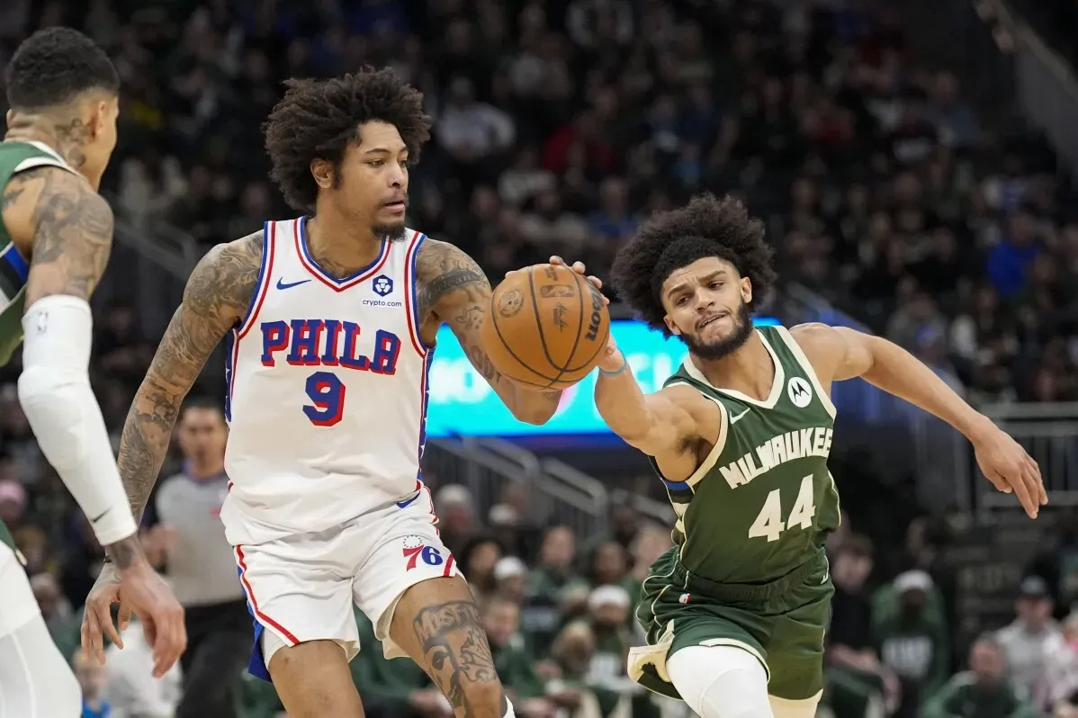 لاعبان من فريق فيلادلفيا 76 يتنافسان على الكرة مع لاعب من ميلووكي باكس خلال مباراة كرة سلة، حيث يظهر الحماس والتنافسية.