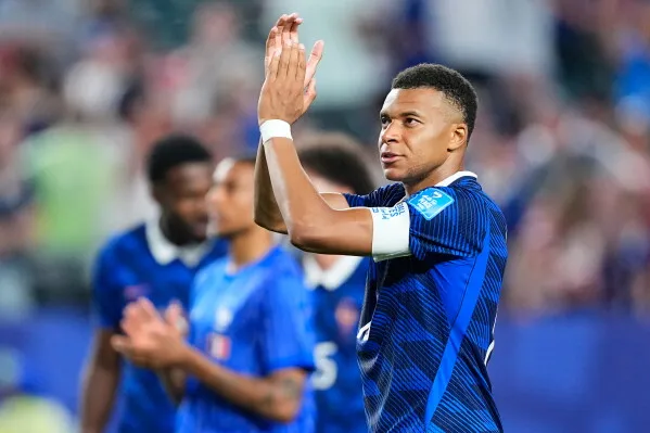 كيليان مبابي يصفق لجماهيره بعد مباراة في كأس العالم، مرتديًا قميص المنتخب الفرنسي الأزرق، وسط أجواء حماسية في الملعب.