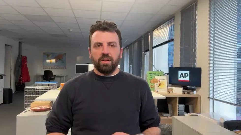 رجل يتحدث في مكتب حديث مع شاشة تعرض شعار وكالة الأنباء AP، في سياق مناقشات حول الأمن الأوروبي والميزانية العسكرية.