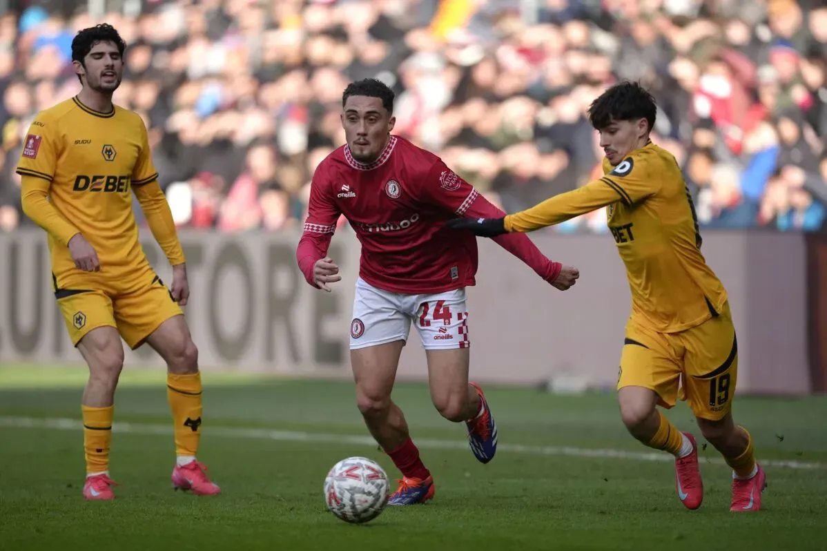 لاعب من فريق بريستول سيتي يرتدي قميصًا أحمر يراوغ لاعبين من ولفرهامبتون خلال مباراة كأس الاتحاد الإنجليزي.