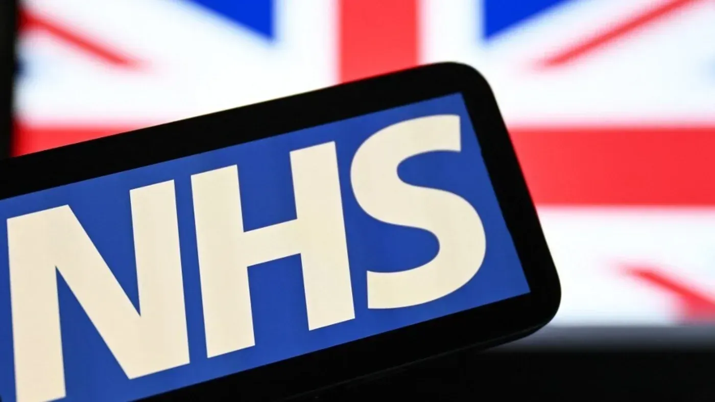 شعار NHS مع العلم البريطاني في الخلفية، يرمز إلى نظام الرعاية الصحية الوطني في المملكة المتحدة وسط جدل حول حرية التعبير.