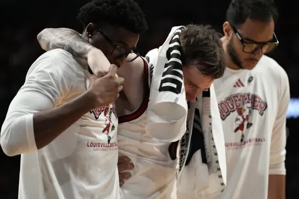 لاعب لويزفيل راين سميث يتلقى الدعم من زملائه بعد إصابته في الكاحل خلال مباراة NCAA، بينما يظهر القلق على وجوههم.