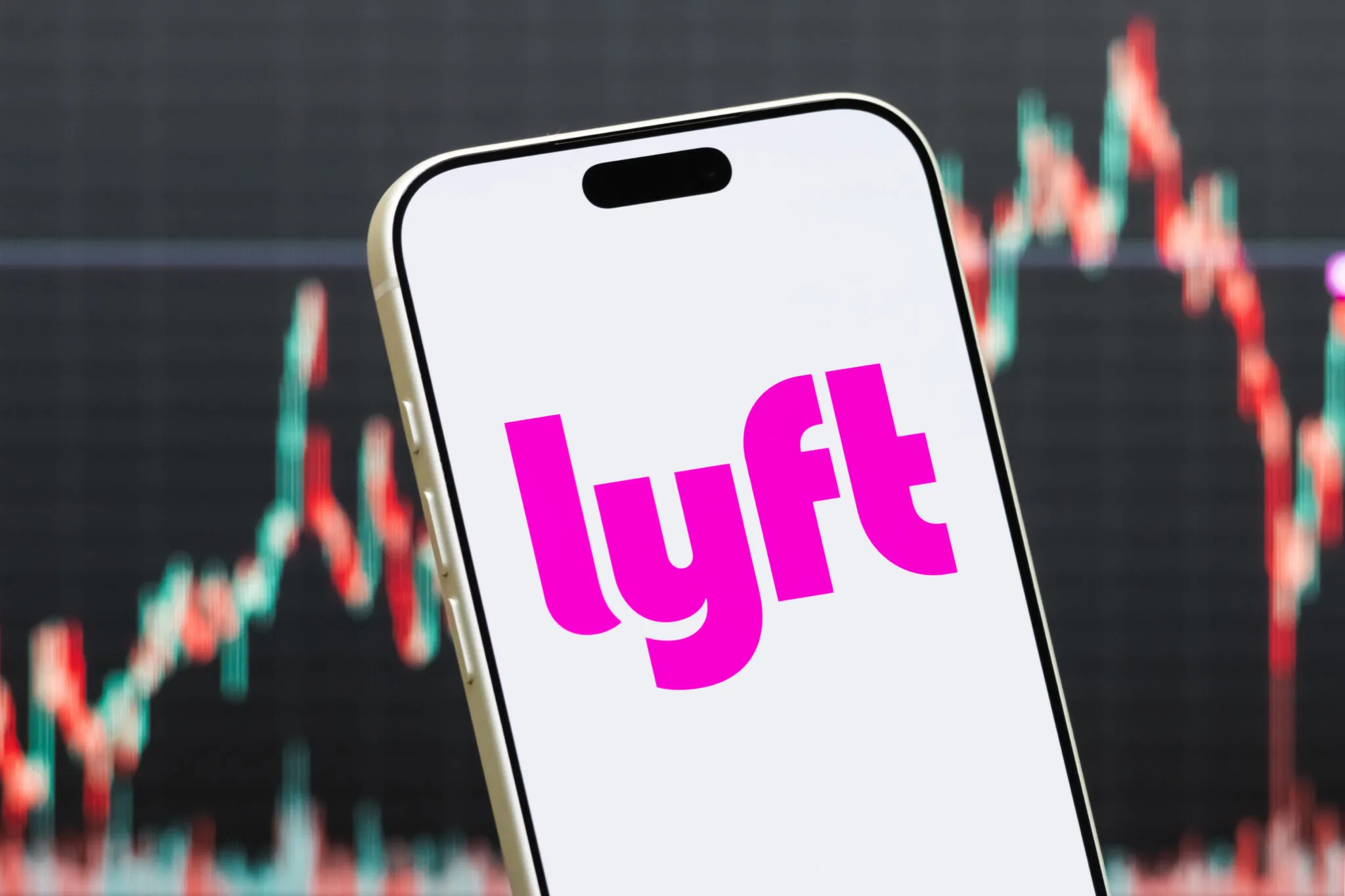 شعار شركة Lyft على شاشة هاتف ذكي مع خلفية رسوم بيانية تعكس تسوية مالية في قضية تصنيف سائقي النقل التشاركي في كاليفورنيا.