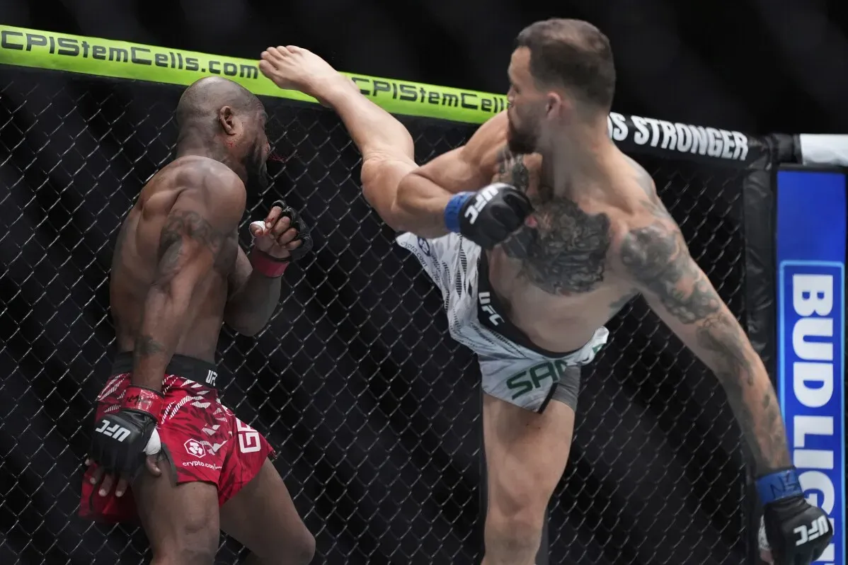 لقطة من نزال في UFC حيث يقوم أحد المقاتلين بركلة قوية نحو خصمه، مع وجود حلبة القتال وشبكة الحماية في الخلفية.