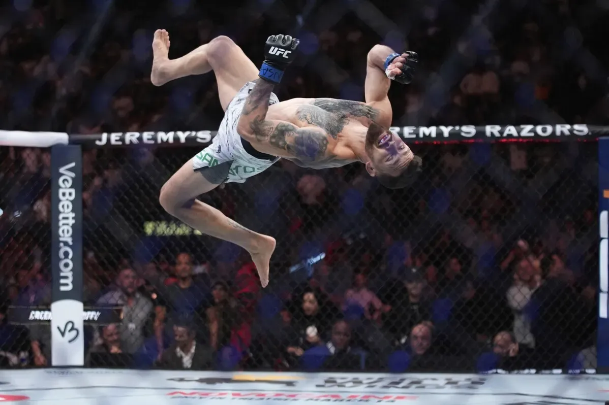 مقاتل يتأرجح في الهواء خلال نزال UFC، يعكس حماس المنافسة في الفنون القتالية المختلطة. الجمهور في الخلفية يشاهد بشغف.
