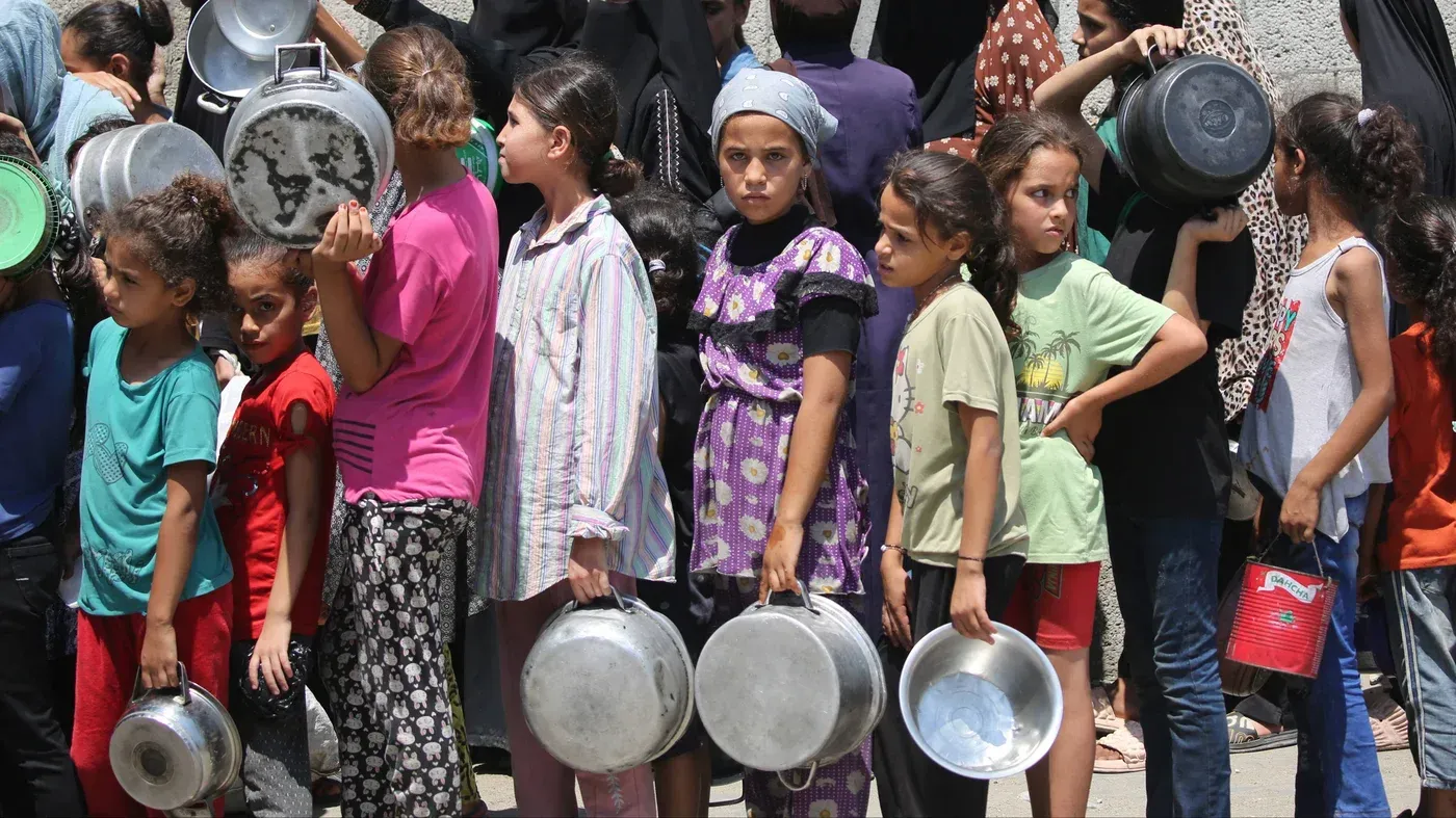 أطفال فلسطينيون في غزة يقفون في صف طويل يحملون أواني للطهي، في ظل أزمة إنسانية بسبب الحصار.