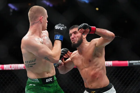 إسلام ماخاشيف يهاجم منافسه إيان ماتشادو جاري في قفص UFC خلال مباراة وزن 170 رطلاً ضمن UFC 330، مع آثار جروح وكدمات على وجهه.