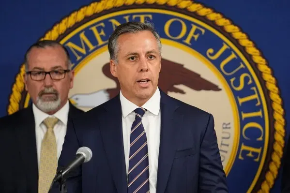 مسؤول حكومي يتحدث خلال مؤتمر صحفي حول حادث إطلاق النار في دالاس، مع وجود شعار وزارة العدل خلفه، في سياق مناقشة الهجوم المستهدف على إدارة الهجرة والجمارك.