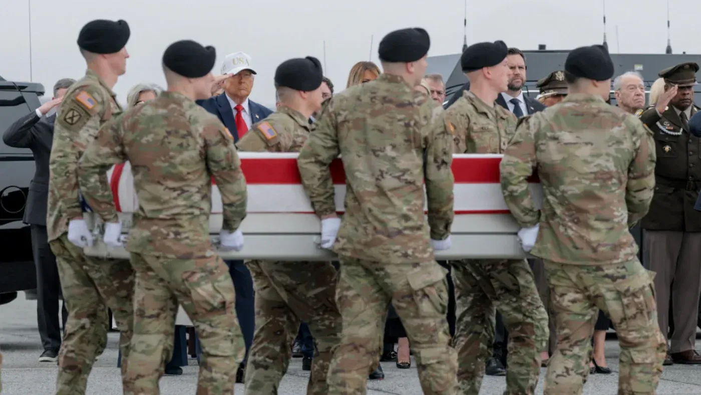 جنود أمريكيون يحملون نعشًا مغطى بالعلم الأمريكي، مع ظهور شخصيات بارزة في الخلفية، وسط أجواء من الحزن والتأمل في تبعات الحرب.
