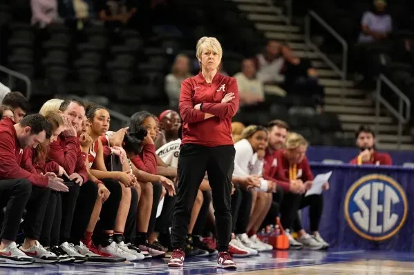 مدربة فريق ألاباما كريستي كاري تراقب اللاعبين على دكة البدلاء خلال مباراة، مع التركيز على التحضيرات لبطولة NCAA.