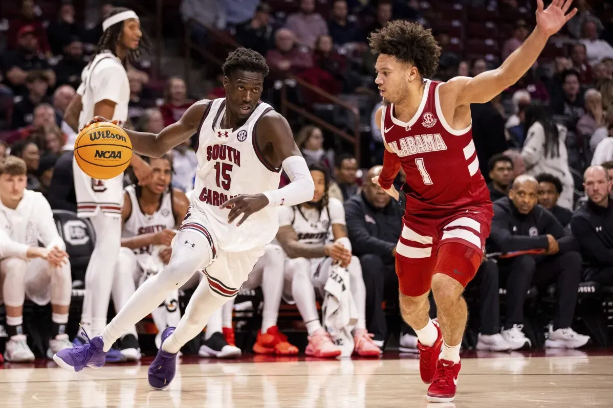 لاعبو كرة السلة من ألاباما وكارولينا الجنوبية يتنافسون على الكرة خلال مباراة NCAA، مع وجود مشجعين في الخلفية.