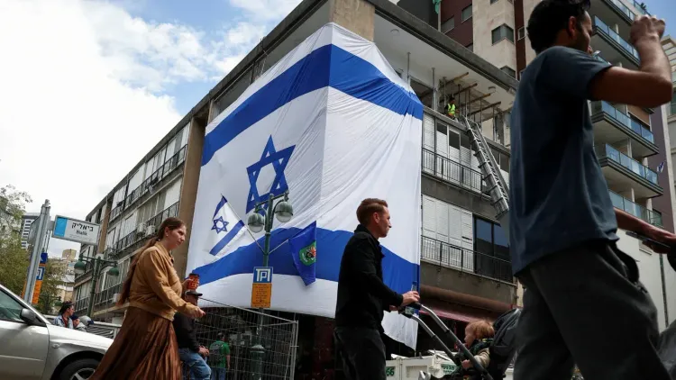 لافتة كبيرة تحمل علم إسرائيل تتدلى من مبنى، بينما يسير المارة في الشارع، مما يعكس أجواء التوتر السياسي في البلاد.