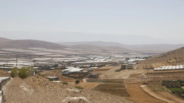 منظر واسع لسهل البقيعة في غور الأردن، يظهر الأراضي الزراعية والمزارع المتضررة من مشروع الجدار الإسرائيلي، مع تدهور المحاصيل بسبب نقص المياه.