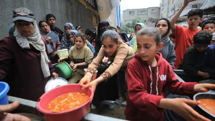 نساء وأطفال فلسطينيون يتجمعون في صف للحصول على الطعام في غزة، وسط أزمة إنسانية متفاقمة نتيجة النزاع المستمر.