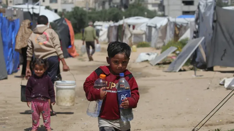 طفل فلسطيني يحمل زجاجات ماء في مخيم نزوح بقطاع غزة وسط ظروف معيشية صعبة وحصار على المياه.