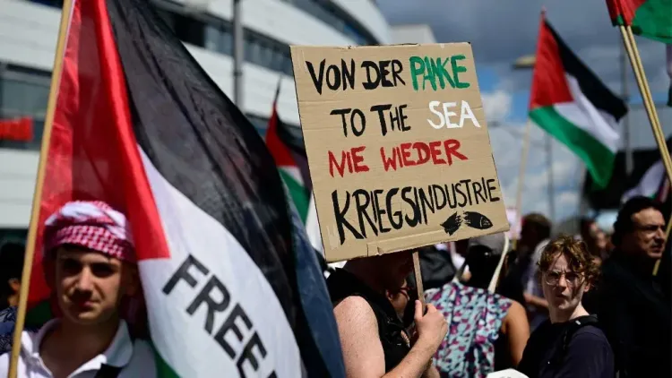 متظاهرون يحملون أعلام فلسطين ولافتة احتجاجية في مظاهرة بألمانيا ضد سياسات إسرائيل في غزة، تعبيراً عن التضامن والدعم الفلسطيني.