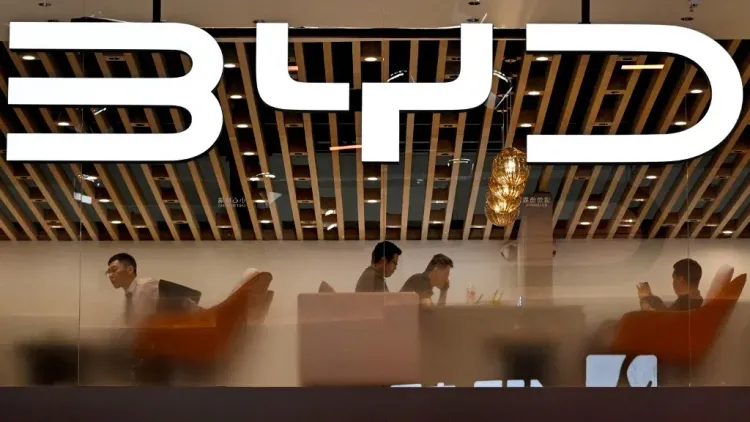 شعار شركة BYD يظهر في واجهة مكتب حديث، مع موظفين يعملون في الداخل، مما يعكس التوجه نحو إنتاج السيارات الكهربائية.