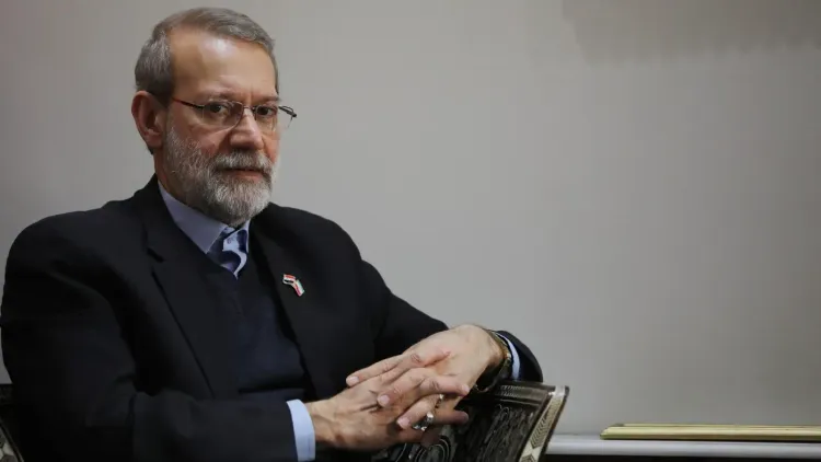 وزير الأمن الإيراني علي لاريجاني يجلس في غرفة، مع تعبير جاد، مرتديًا بدلة داكنة وقميصًا أزرق، يعكس تأثيره في السياسة الإيرانية.