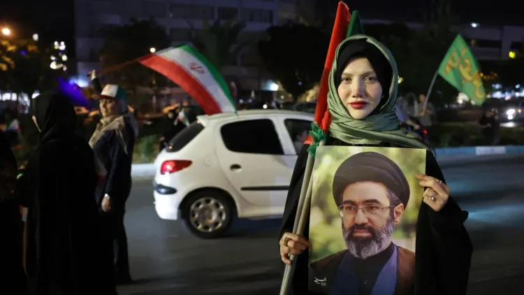 امرأة تحمل صورة لشخصية سياسية إيرانية، بينما ترفع علم إيران في تجمع ليلي حاشد وسط طهران، تعبيراً عن الدعم الوطني.