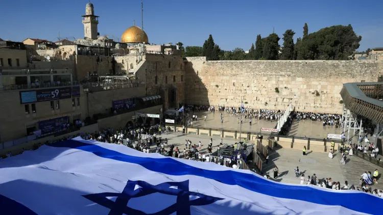 صورة لحي البلدة القديمة في القدس، تظهر حائط البراق والمصلين، مع العلم الإسرائيلي في المقدمة، تعكس التوترات الحالية حول مصادرة العقارات الفلسطينية.