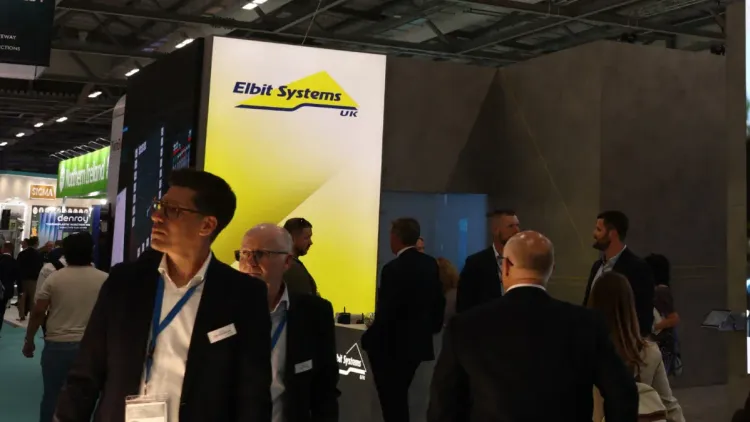 وفد زوار في معرض دفاعي أمام شعار شركة Elbit Systems الإسرائيلية المتخصصة في الطائرات المسيّرة وأنظمة المراقبة.