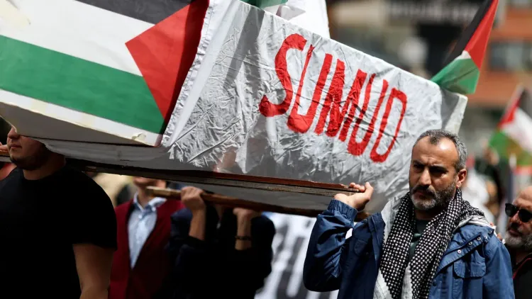 محتجون يحملون نعشًا مكتوبًا عليه "صمود" خلال مظاهرة تضامن مع غزة، مع أعلام فلسطينية ترفرف في الخلفية.