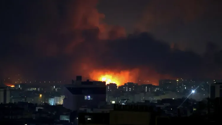 تظهر الصورة مشهدًا ليليًا لمدينة تتعرض لهجوم، حيث تتصاعد ألسنة اللهب والدخان الكثيف في السماء، مما يعكس تصاعد التوترات في الشرق الأوسط.