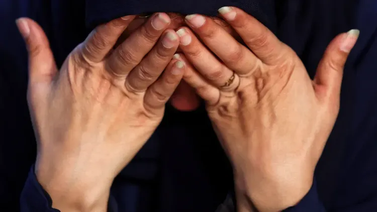 امرأة فلسطينية تغطي وجهها بيديها تعبيرًا عن الألم والقلق، في سياق معاناة العائدين إلى غزة بعد الاستجواب من القوات الإسرائيلية.