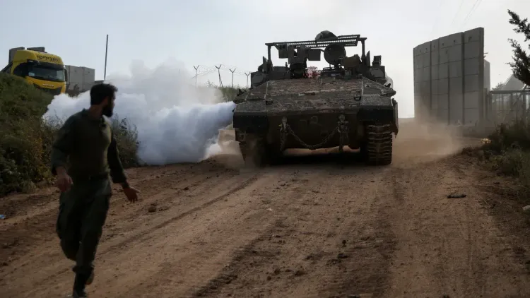 دبابة إسرائيلية تطلق دخاناً على طريق ترابي في جنوب لبنان، بينما يركض جندي نحوها، مما يعكس تصاعد التوترات العسكرية في المنطقة.