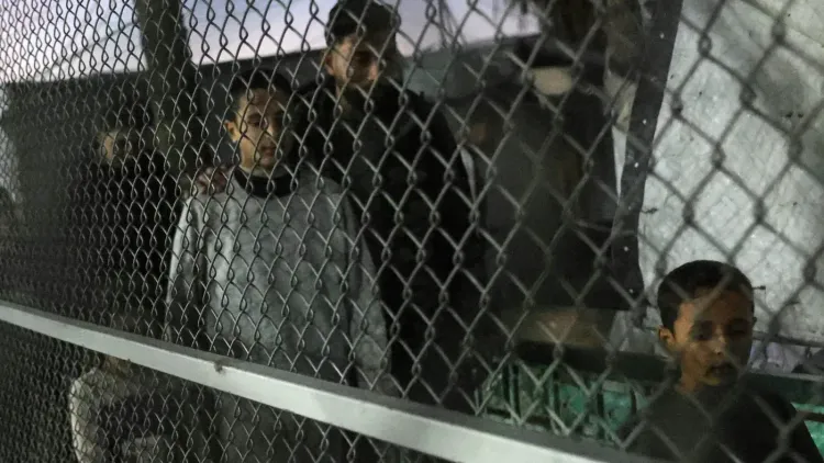 أطفال فلسطينيون يقفون خلف سياج معدني في مركز احتجاز، يعكس الأوضاع الصعبة التي يواجهها الأسرى في ظل التوترات الحالية.