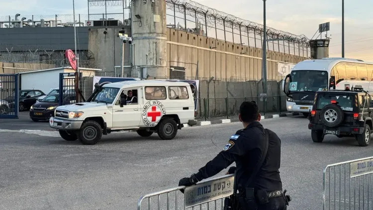 سيارة تابعة للصليب الأحمر تمر أمام سجن محاط بأسلاك شائكة، حيث يُظهر الوضع الأمني المشدد في مراكز احتجاز المعتقلين الفلسطينيين.