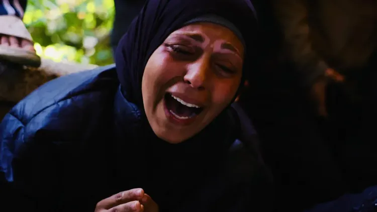 امرأة ترتدي الحجاب تعبر عن حزن عميق أثناء تأبين ضحايا الحرب في غزة، مع خلفية غير واضحة تعكس مشاعر الألم والمعاناة.