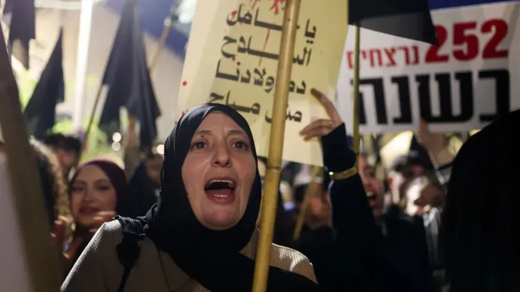 محتجون فلسطينيون في مظاهرة ضد العنف في إسرائيل، يحملون لافتات تعبر عن مطالبهم، وسط أجواء من التوتر والإصرار.