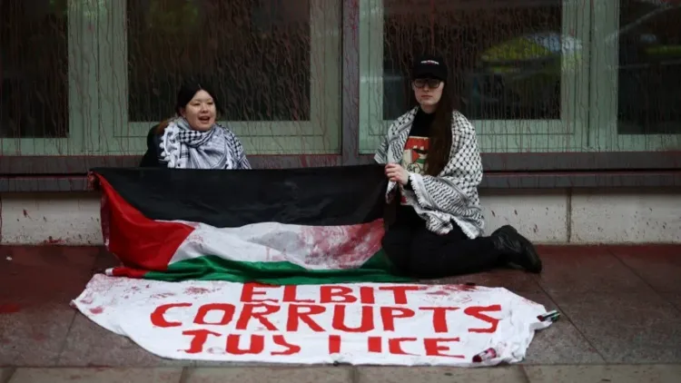 نشطاء يحملون علم فلسطين ولافتة مكتوب عليها "إلبيت تفسد العدالة" خلال احتجاج ضد شركة إلبيت سيستمز في لندن.