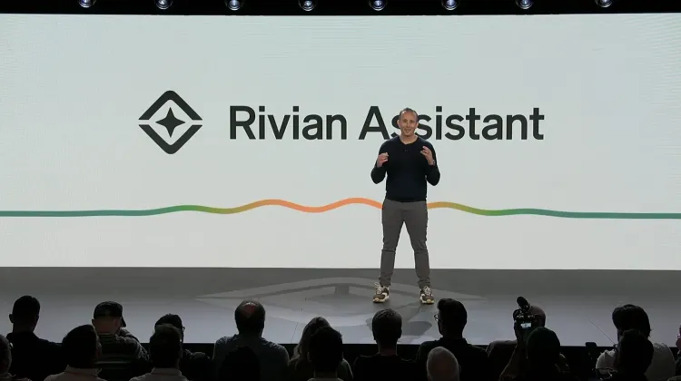 رجل يقدم مساعد Rivian الصوتي بالذكاء الاصطناعي أمام جمهور، مع شعار Rivian Assistant على الشاشة في عرض تقني.