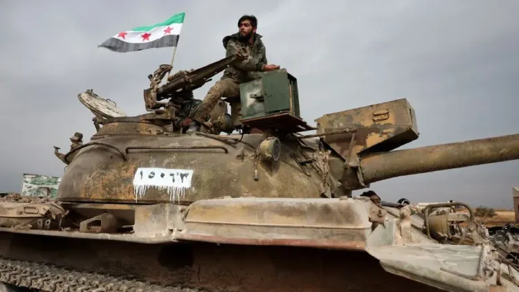مقاتل من قوات المعارضة السورية يجلس على دبابة قديمة، حاملاً علم الثورة السورية، في سياق الاشتباكات المستمرة في الرقة.